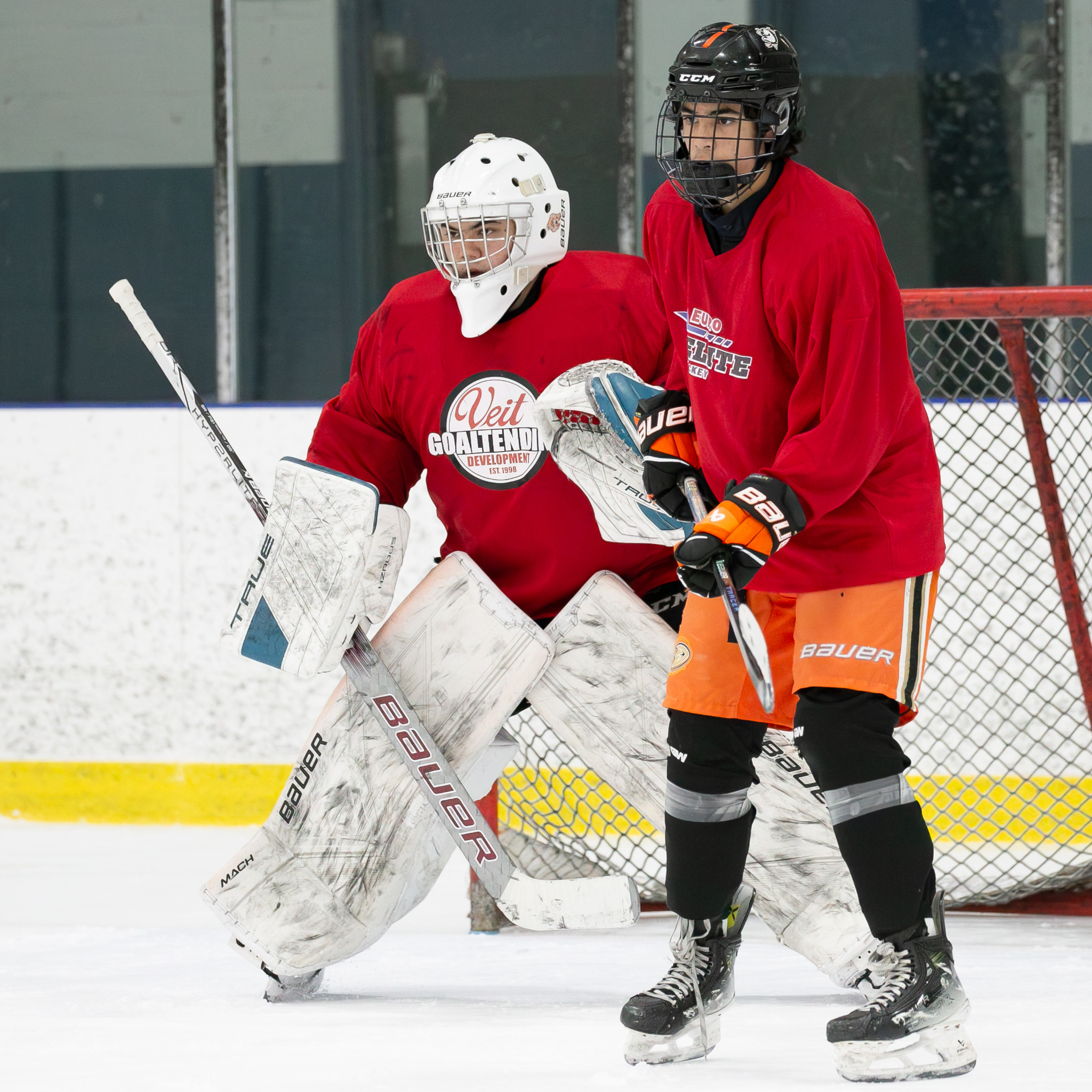 Euro Elite Hockey player and goalie in red jerseys beside the net during an on-ice session